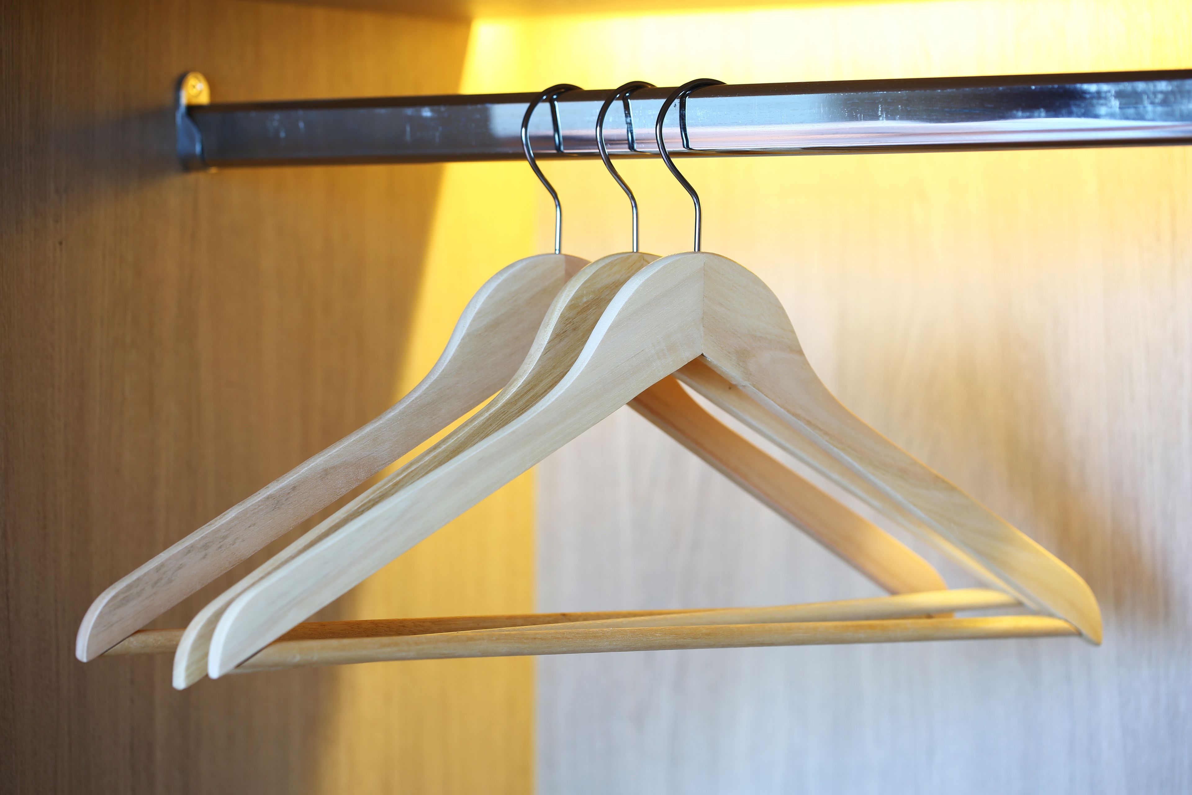 A wooden hanger rack with two hangers against a wooden wall.