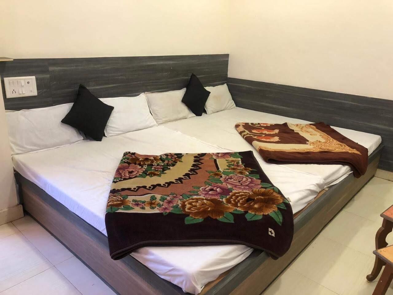 A bed with a dark headboard, white bedding, and two decorative pillows. A floral-patterned throw blanket is draped over the bed.