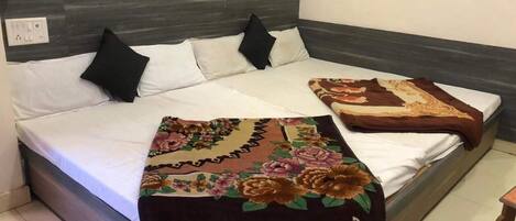 A bed with a dark headboard, white bedding, and two decorative pillows. A floral-patterned throw blanket is draped over the bed.