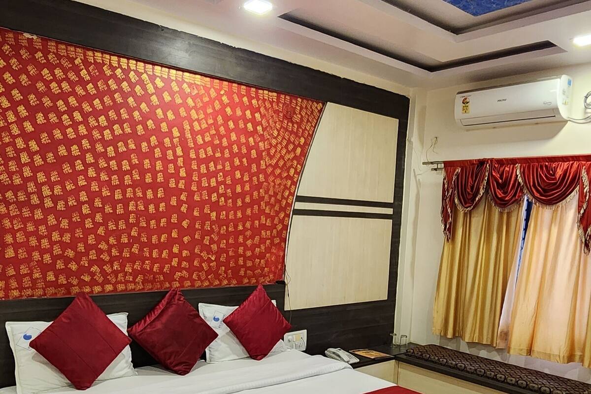 A hotel room with a large bed, red and white bedding, a ceiling fan, an air conditioning unit, and a red patterned wall.