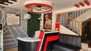 A reception area with a modern design, including a black and red reception desk, a marble-topped counter, a green wall with plants, a map, and a staircase with wooden railings. - Hotel Satpura Safari (Pipariya)