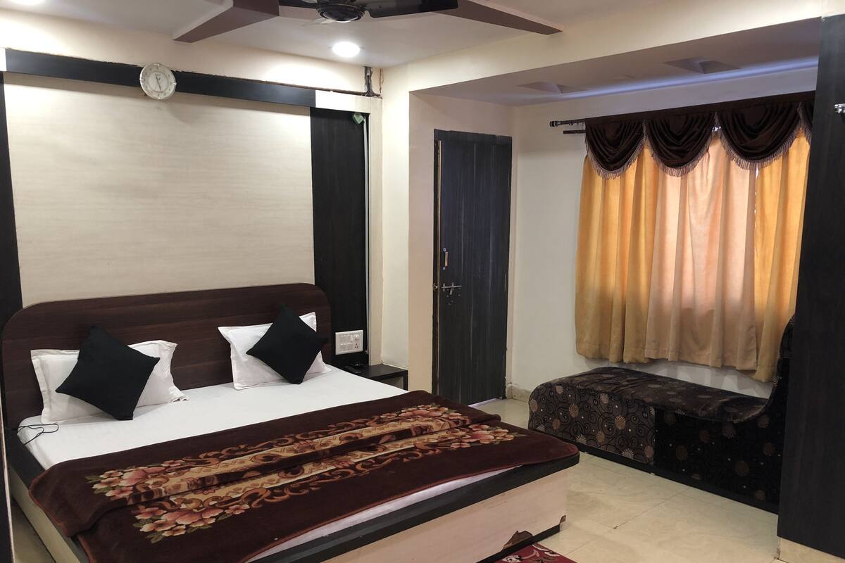 A bedroom with a bed, a bedside table, a window with curtains, a door, and a ceiling fan.