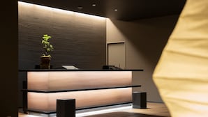 A reception desk with a potted plant, a wooden counter, and a bench.