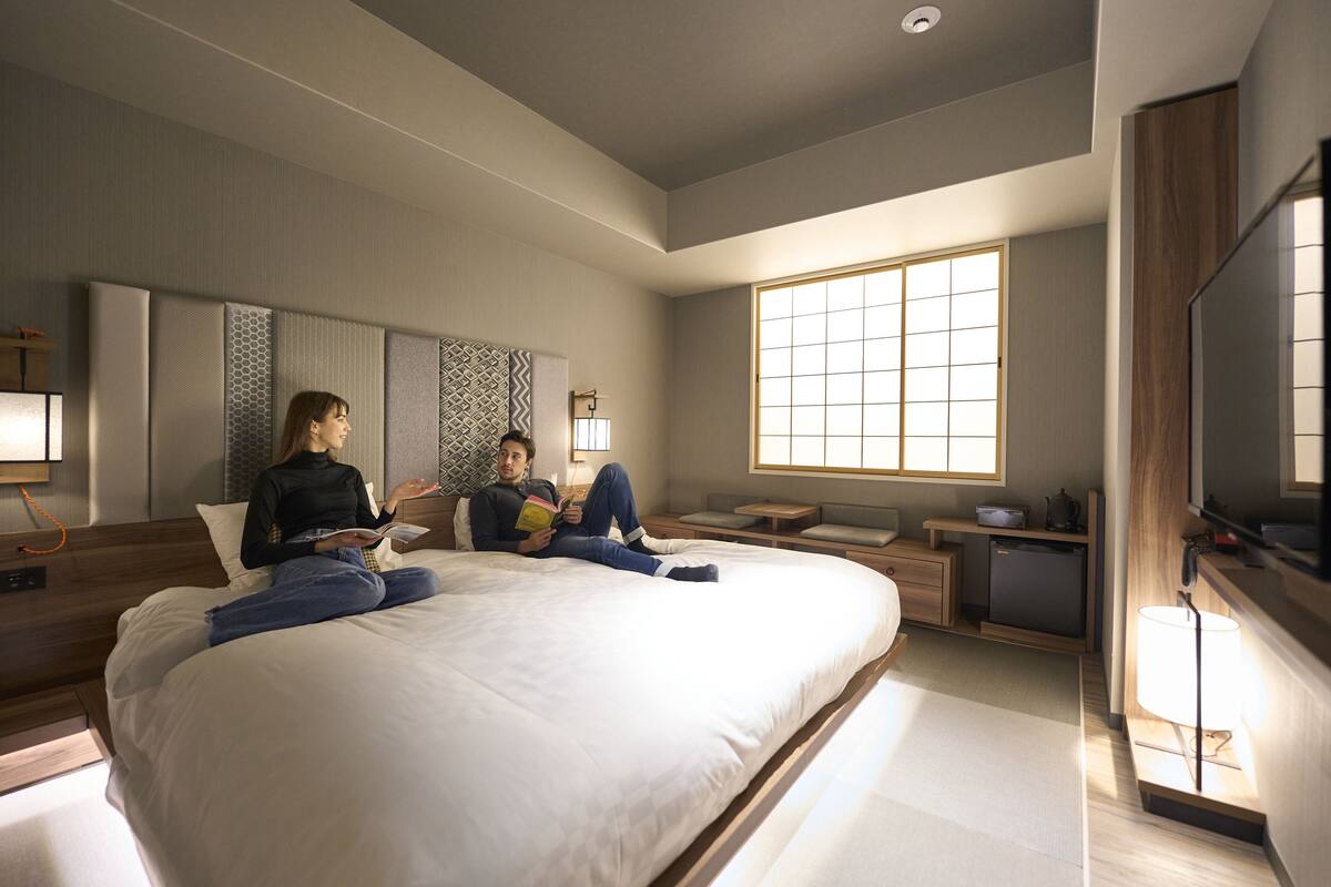 A modern bedroom with a large bed, bedside tables, a TV, and a window.