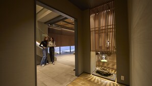 A modern interior with a wooden floor, a glass display case with a sculpture, and a view of a building outside.