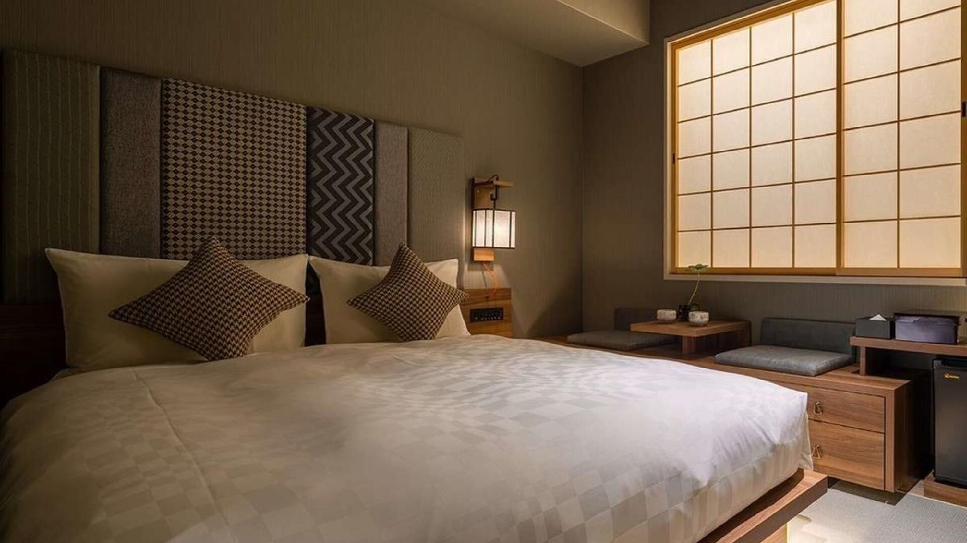 Une chambre d’hôtel avec un grand lit, des tables de chevet, une commode, un bureau et une fenêtre donnant sur un beau paysage.