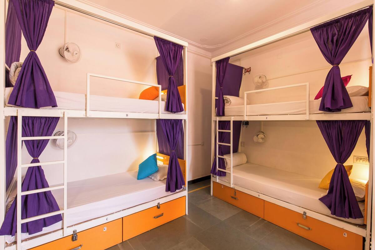 Un dormitorio con camas literas, cajones para guardar objetos color naranja y cortinas moradas.