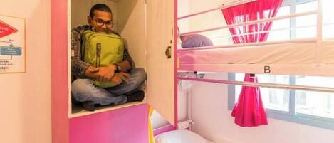 A bunk bed room with pink and white walls, a window with pink curtains, and a person sitting in a doorway.