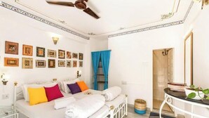 Une chambre à coucher bien rangée, avec un lit, des tables de chevet, un ventilateur de plafond et un mur décoré de tableaux encadrés.