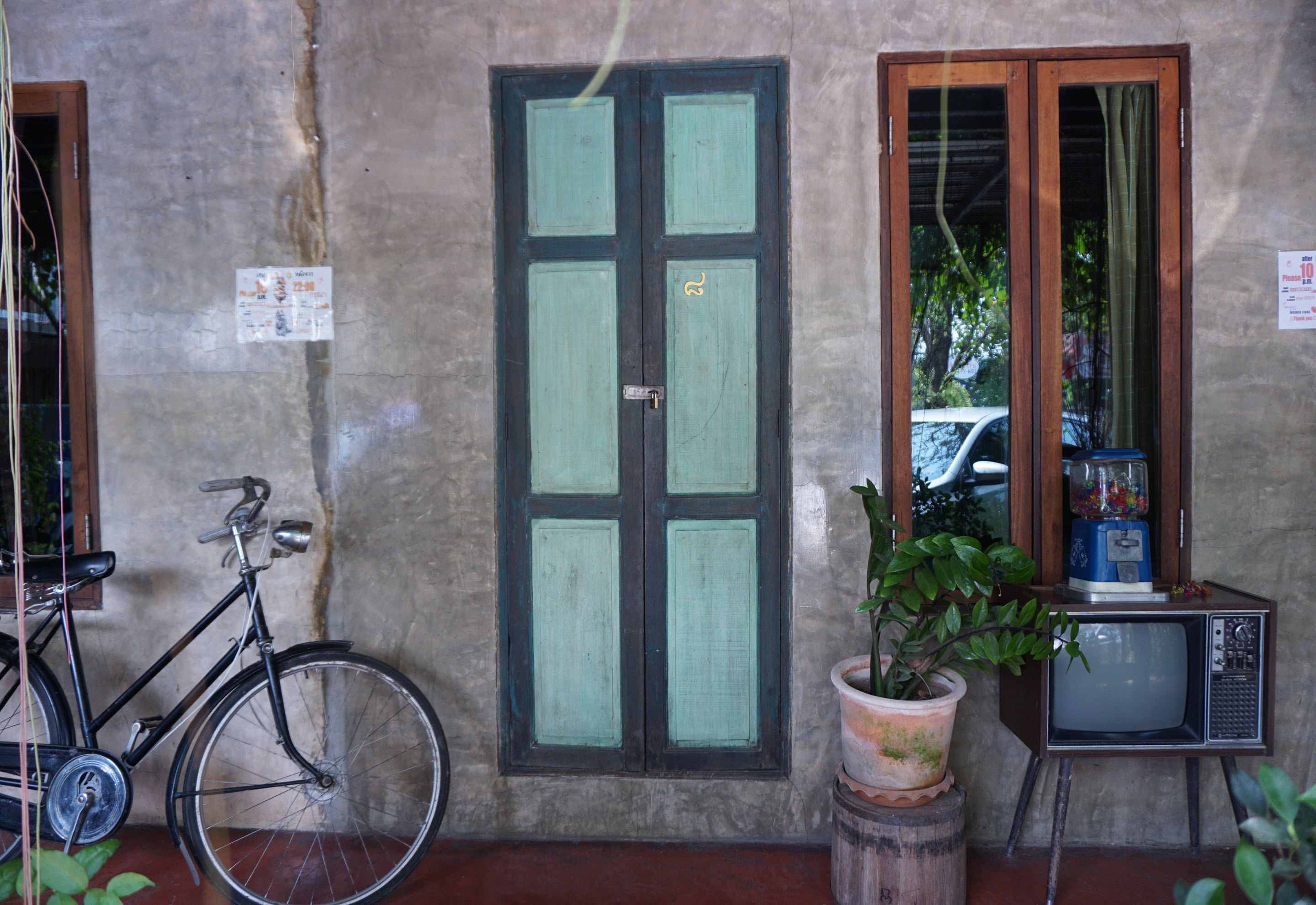 A bicycle parked next to a door, a potted plant, and a vintage television set.