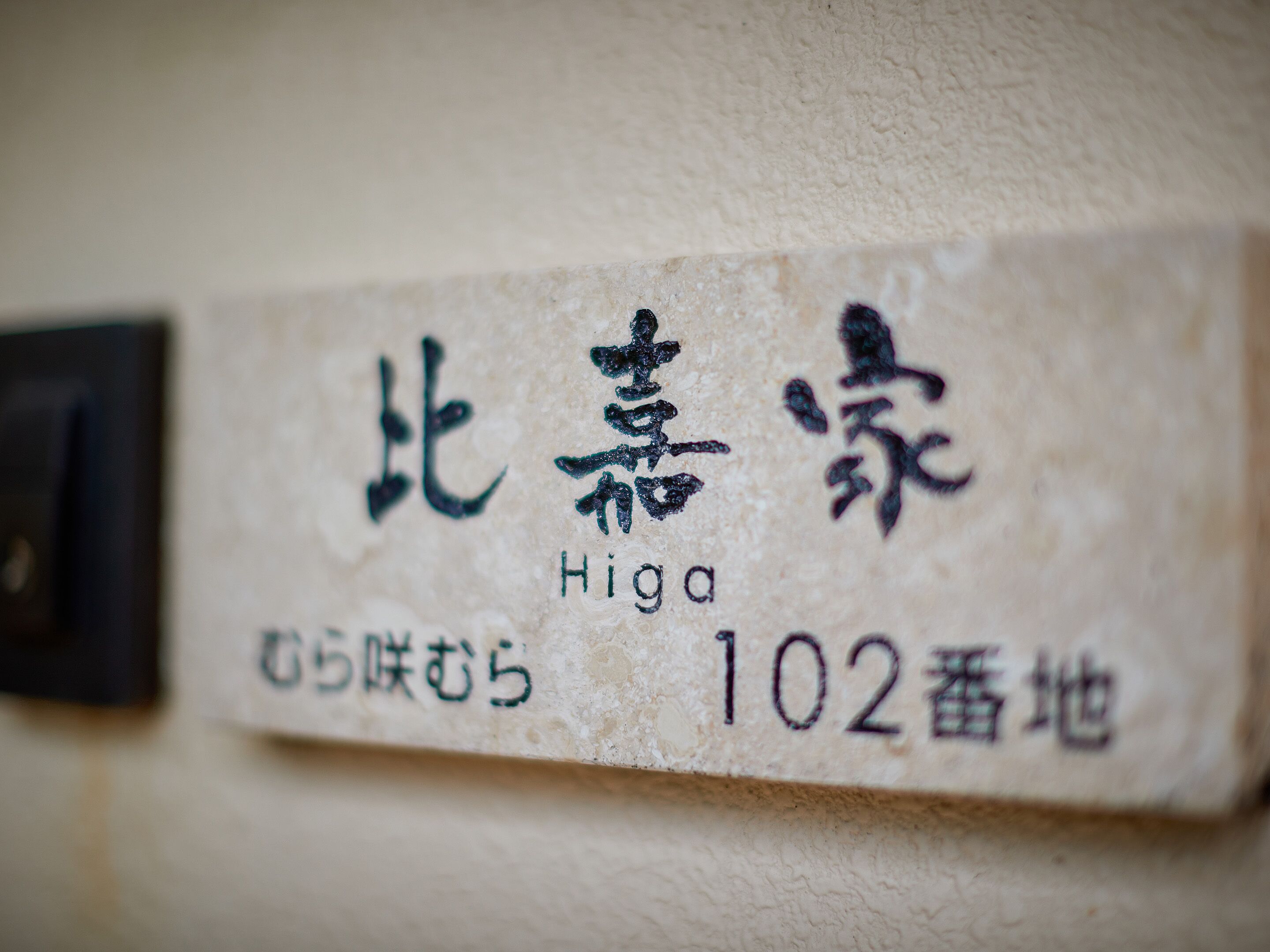 A close-up of a Japanese address sign with the name "Higa" and the number "102".