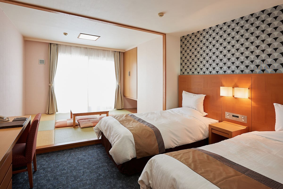 Quarto de hotel com duas camas, uma escrivaninha e vista para o exterior.