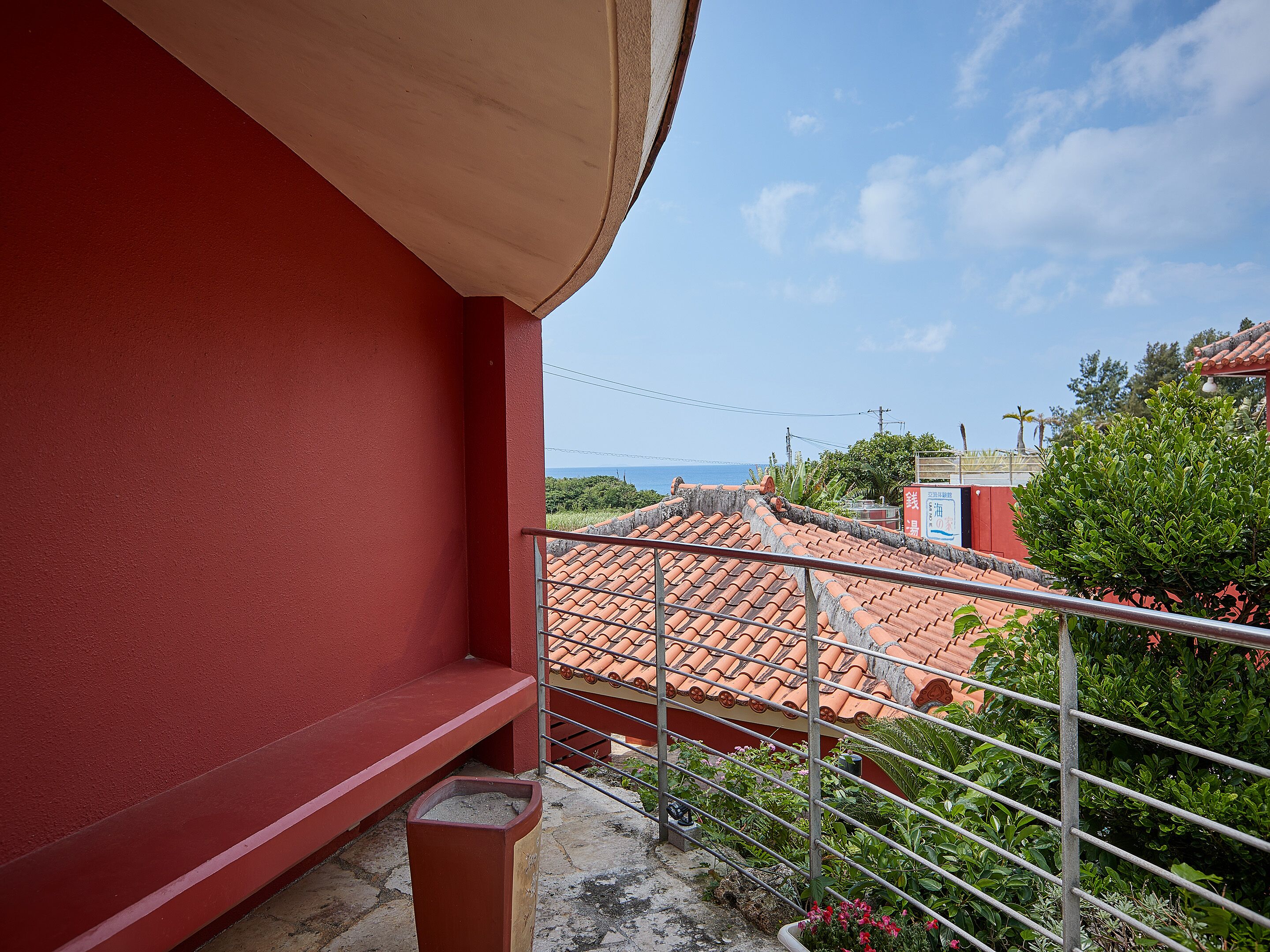A balcony with a red wall, a tiled roof, and a view of the sea.