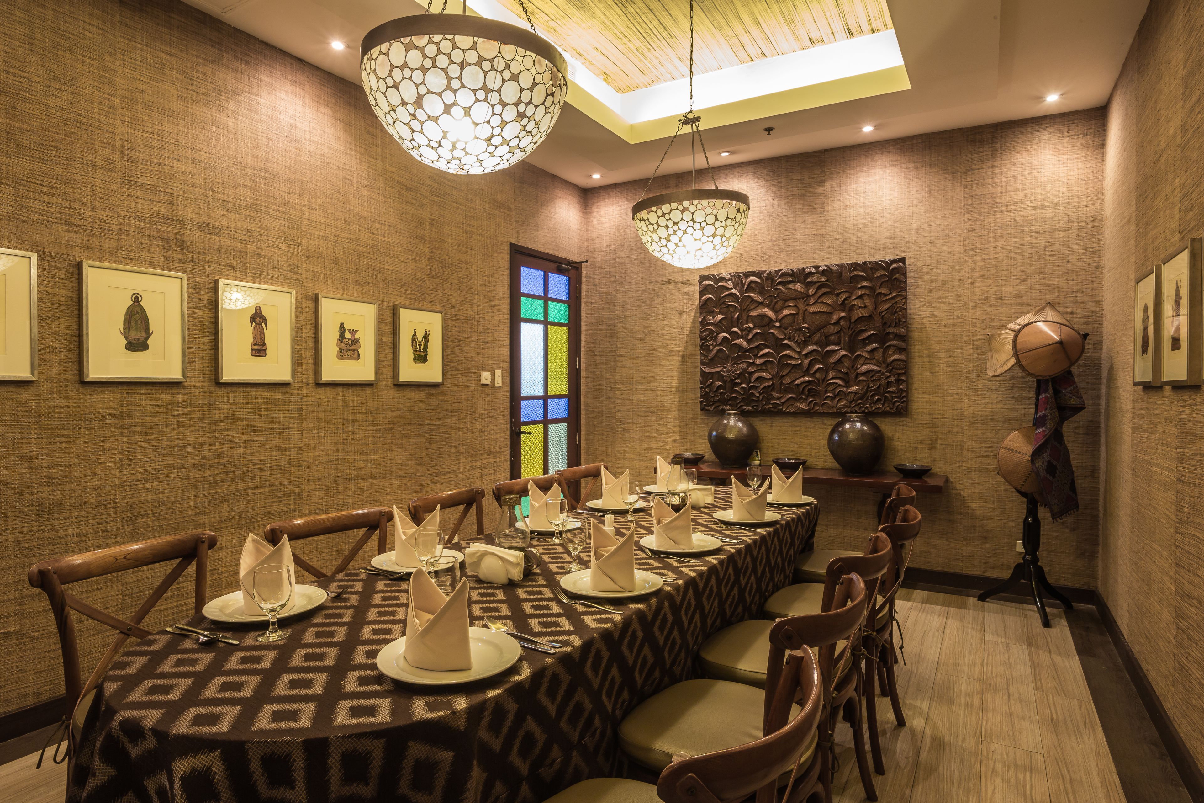 A dining area with a long table set for a meal, framed artwork on the walls, and a decorative ceiling light.