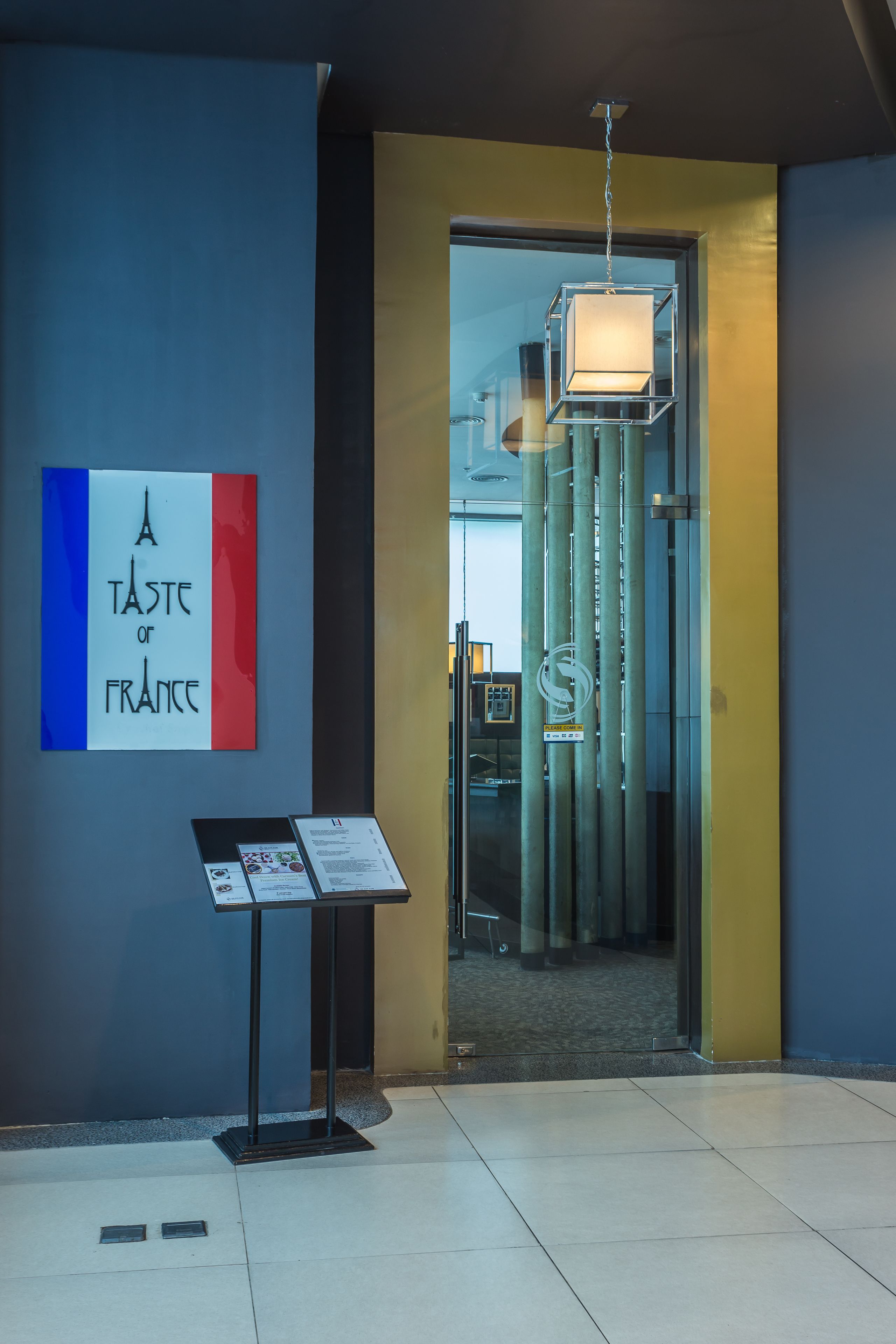 A modern interior with a glass door leading to a room, a sign reading "A Taste of France", and a menu stand.