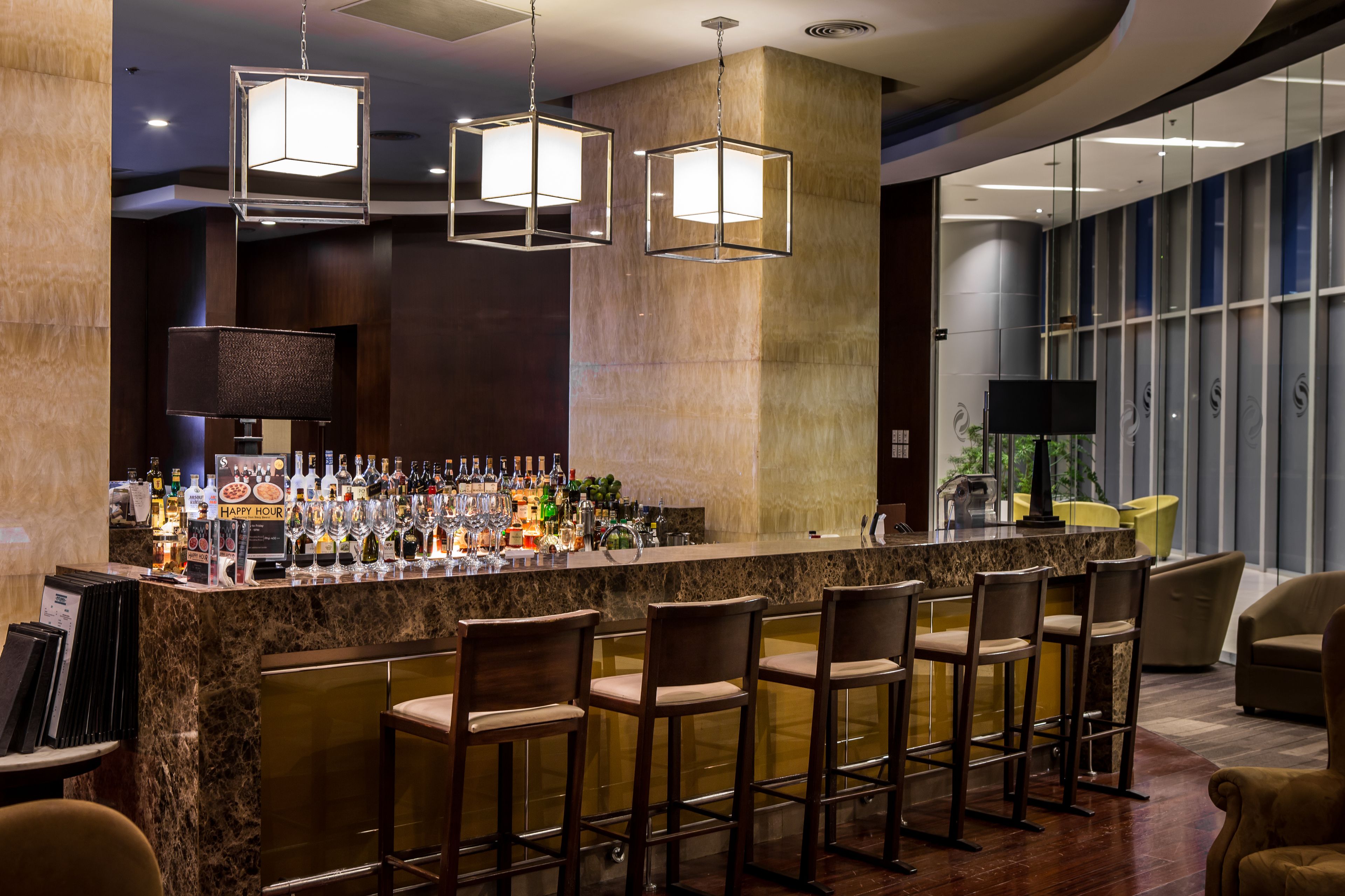 A bar area with a marble countertop, multiple bar stools, and a variety of bottles and glasses.