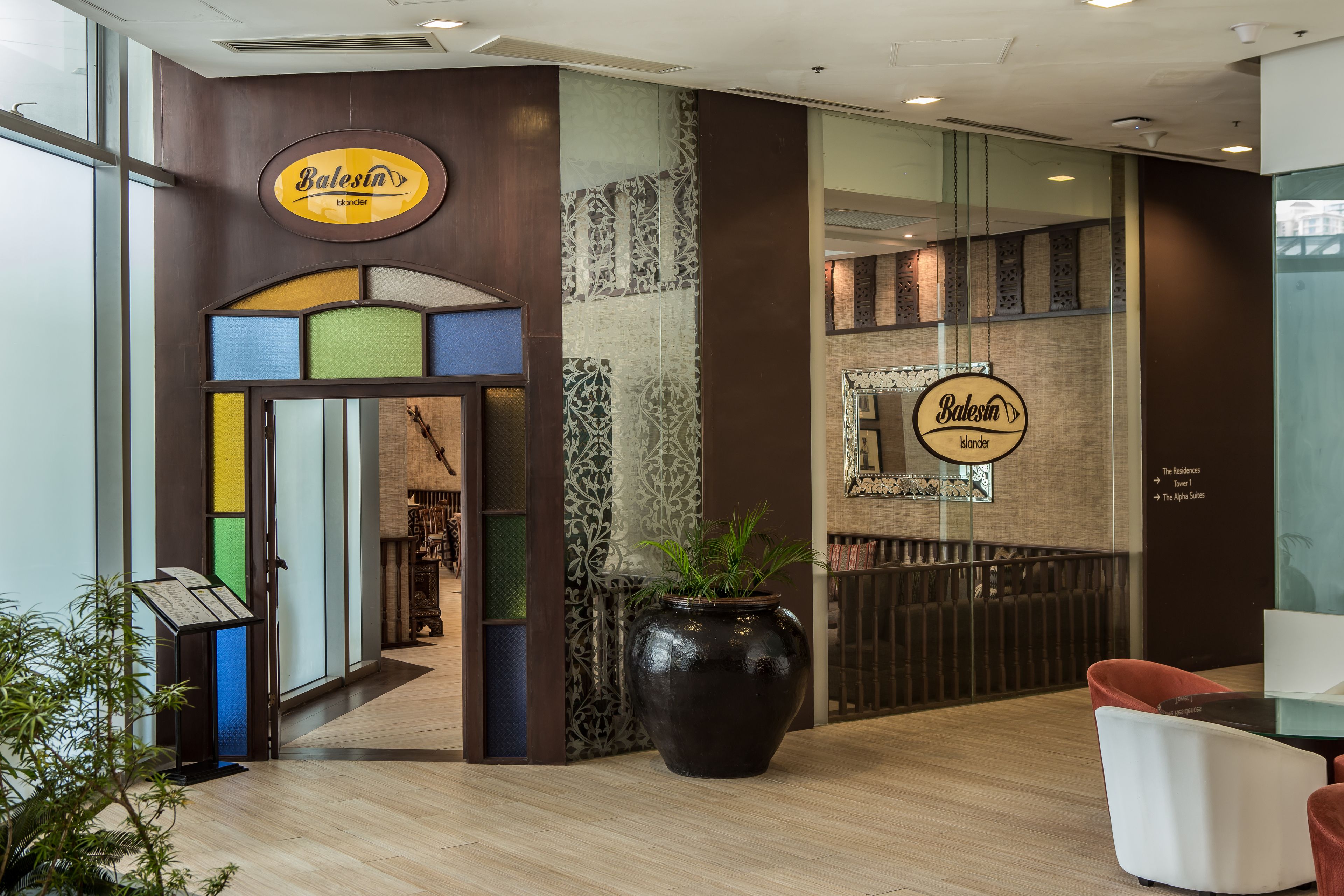A hotel lobby with a large black vase, a reception desk, and a sign reading "Balesin Islander".