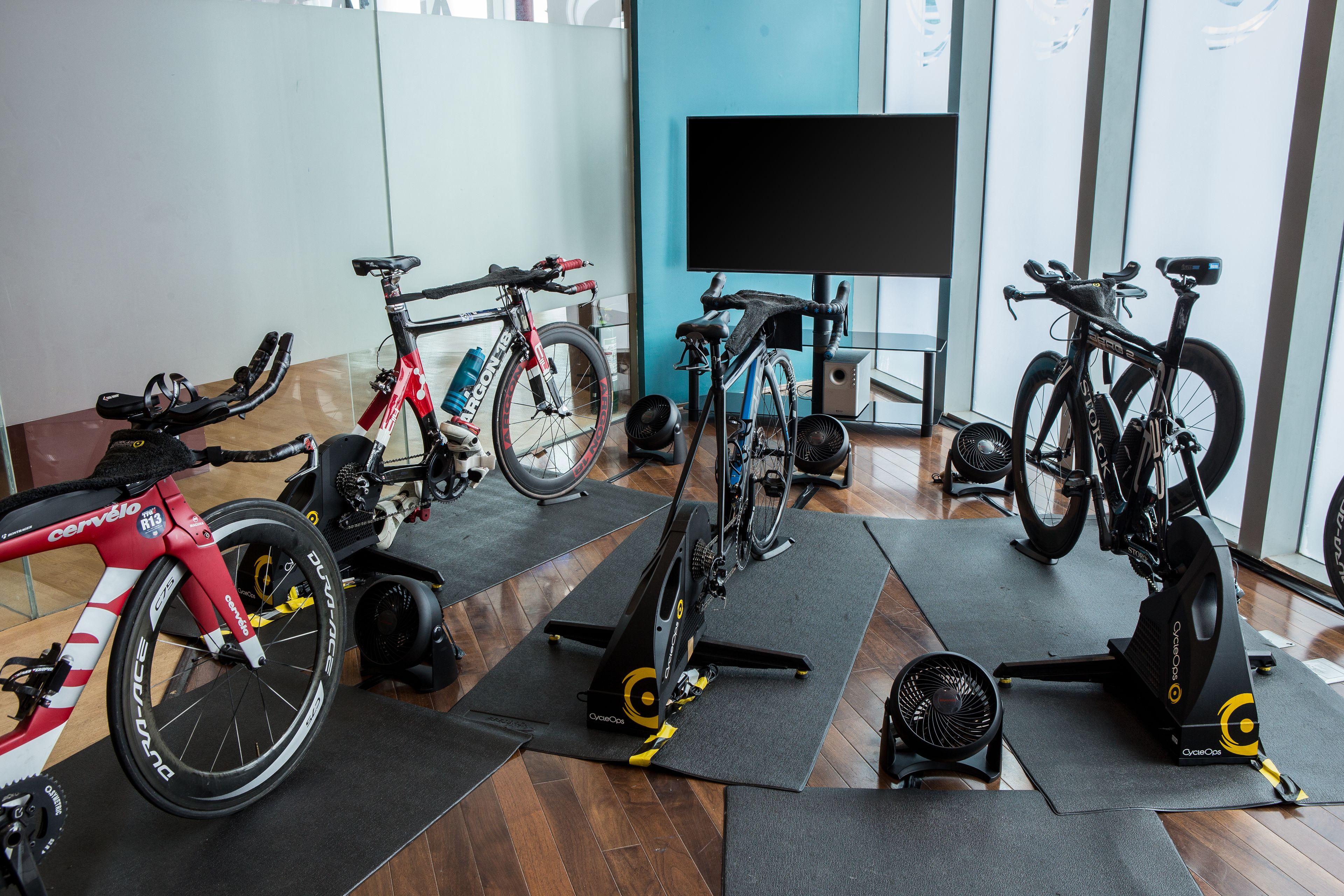A gym with stationary bikes, exercise equipment, and a large TV screen.