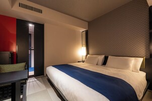 A hotel room with a large bed, a bedside table, a nightstand, a mirror, and a red accent wall.