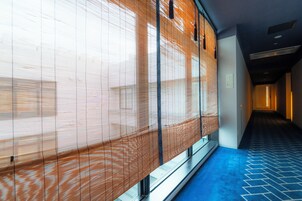A hallway with patterned blinds, a blue carpet, and a staircase leading to another level.