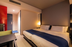 A hotel room with a bed, a desk, a chair, and a wardrobe.