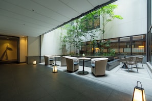 A modern indoor seating area with tables and chairs, a large window overlooking a courtyard with greenery. - Hotel Resol Trinity Kyoto (Kyoto)