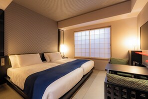 Een hotelkamer met een bed, nachtkastje, lamp en uitzicht door een raam.