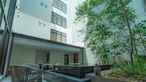 A modern outdoor seating area with a stone bench and a table, surrounded by greenery and a building facade.
