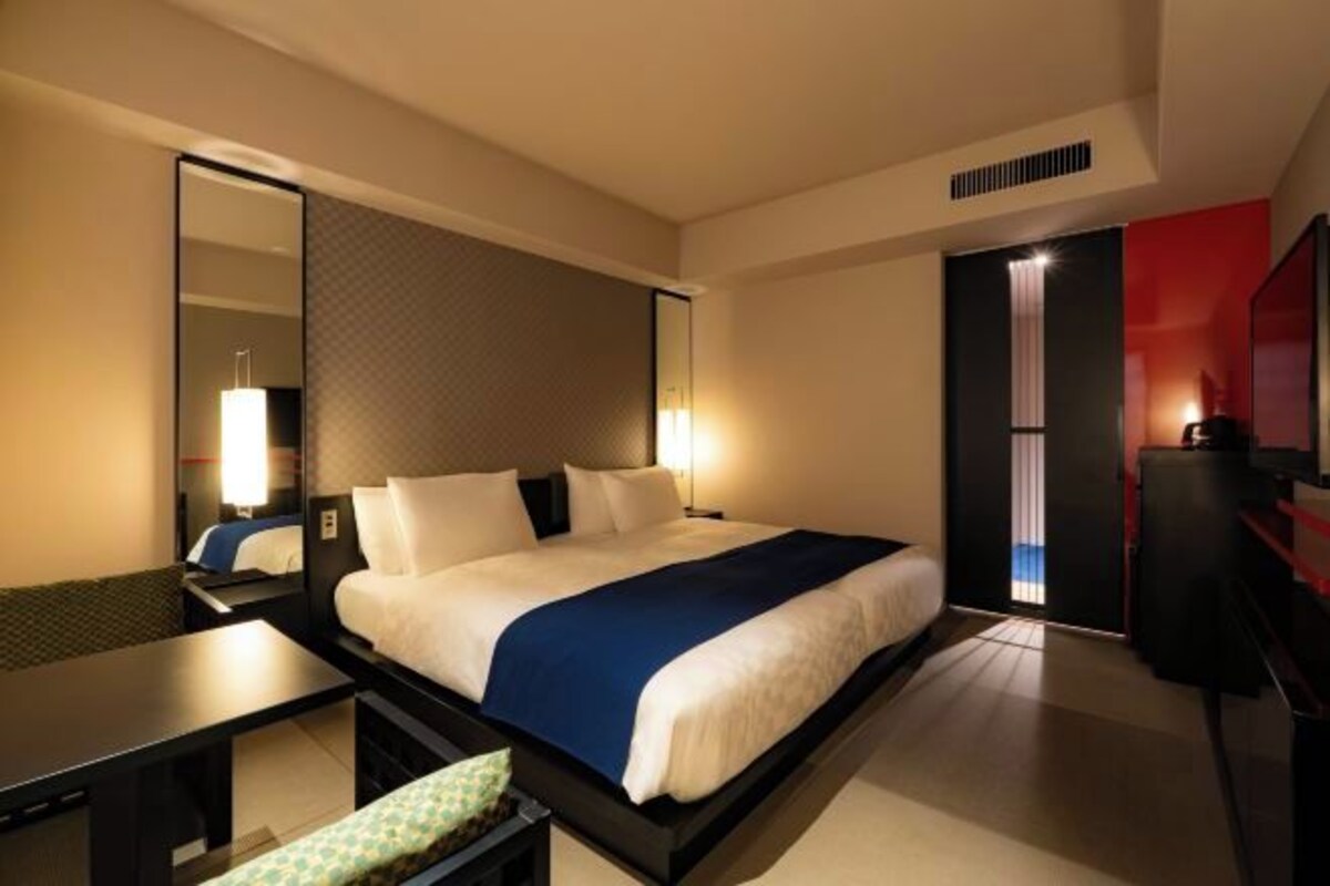 A hotel room with a bed, bedside table, lamp, and a mirror.
