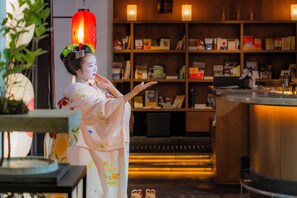 A traditional interior with a person in a kimono, a bookshelf, and a counter. - Hotel Resol Trinity Kyoto (Kyoto)