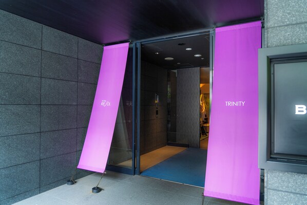 Entrada de un hotel con puerta de cristal y letreros rosas.