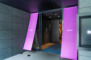Entrada de un hotel con puerta de cristal y letreros rosas.