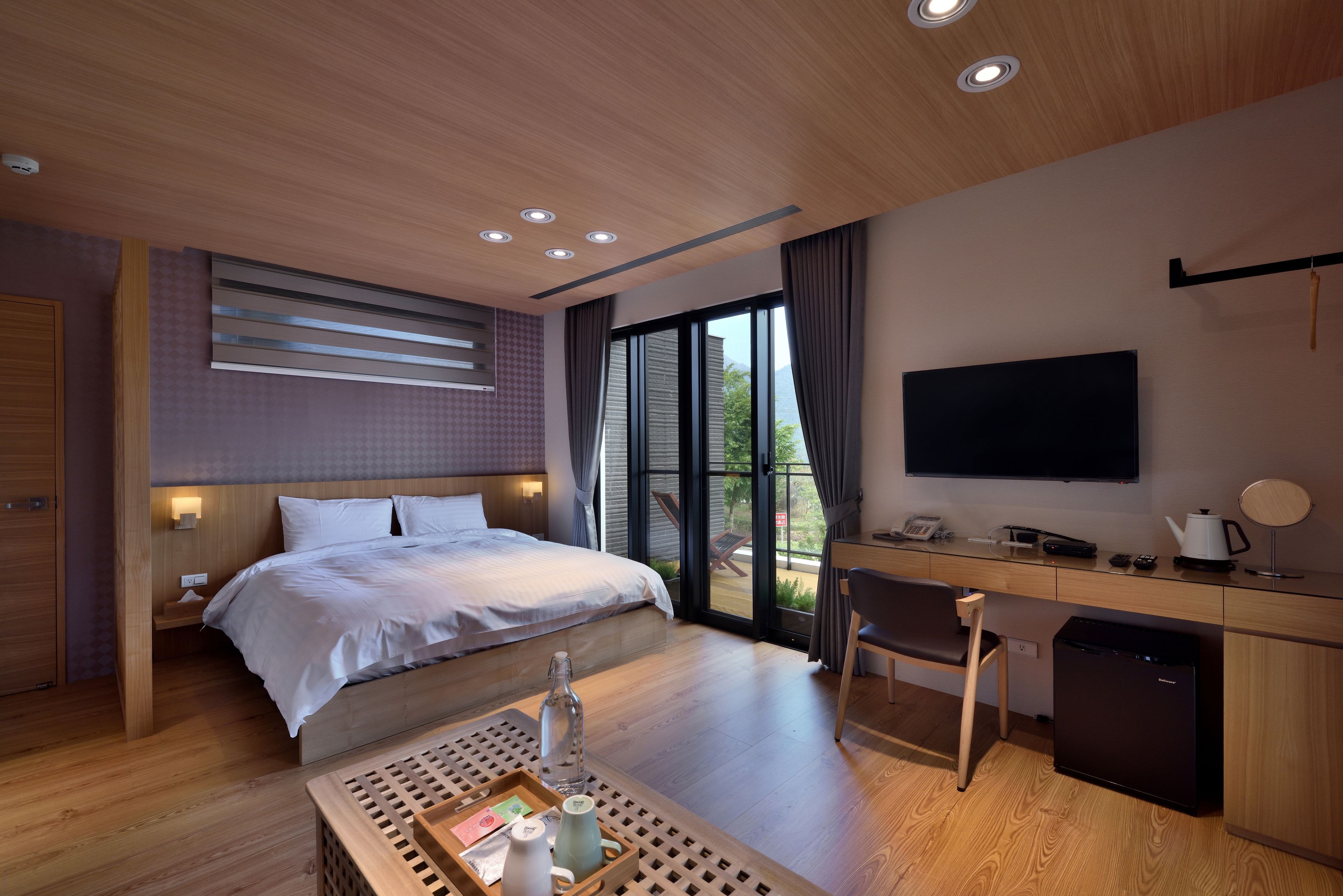A modern hotel room with a large bed, a desk with a computer, a television, and a small refrigerator.