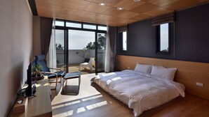 A modern hotel room with a large bed, a desk with a computer, a chair, and a balcony with a view of the city. - Shanyifang Resort (Yuanshan)