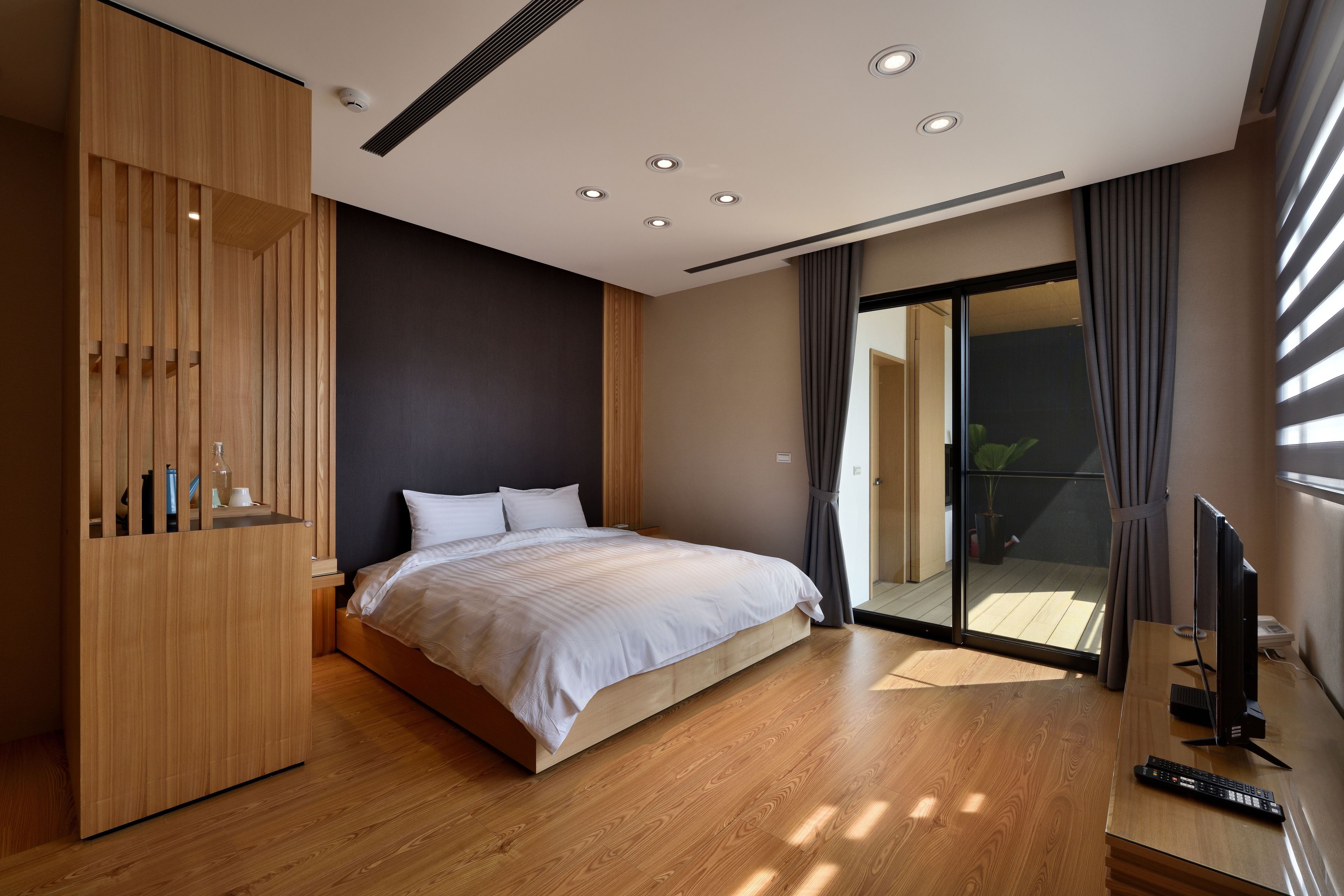 A modern bedroom with a large bed, wooden wardrobe, and a TV on a desk.