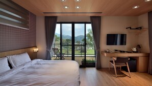 A modern hotel room with a large bed, a desk with a flat-screen TV, and a view of the outdoors. - Shanyifang Resort (Yuanshan)