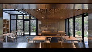 A modern dining area with wooden tables and chairs, large windows, and a view of the outdoors. - Shanyifang Resort (Yuanshan)