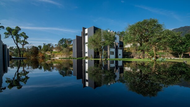 A modern building with a reflection in the water, surrounded by trees and a clear sky. - Shanyifang Resort (Yuanshan)