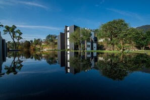 Un edificio moderno con su reflejo en el agua, rodeado de árboles y un cielo despejado.