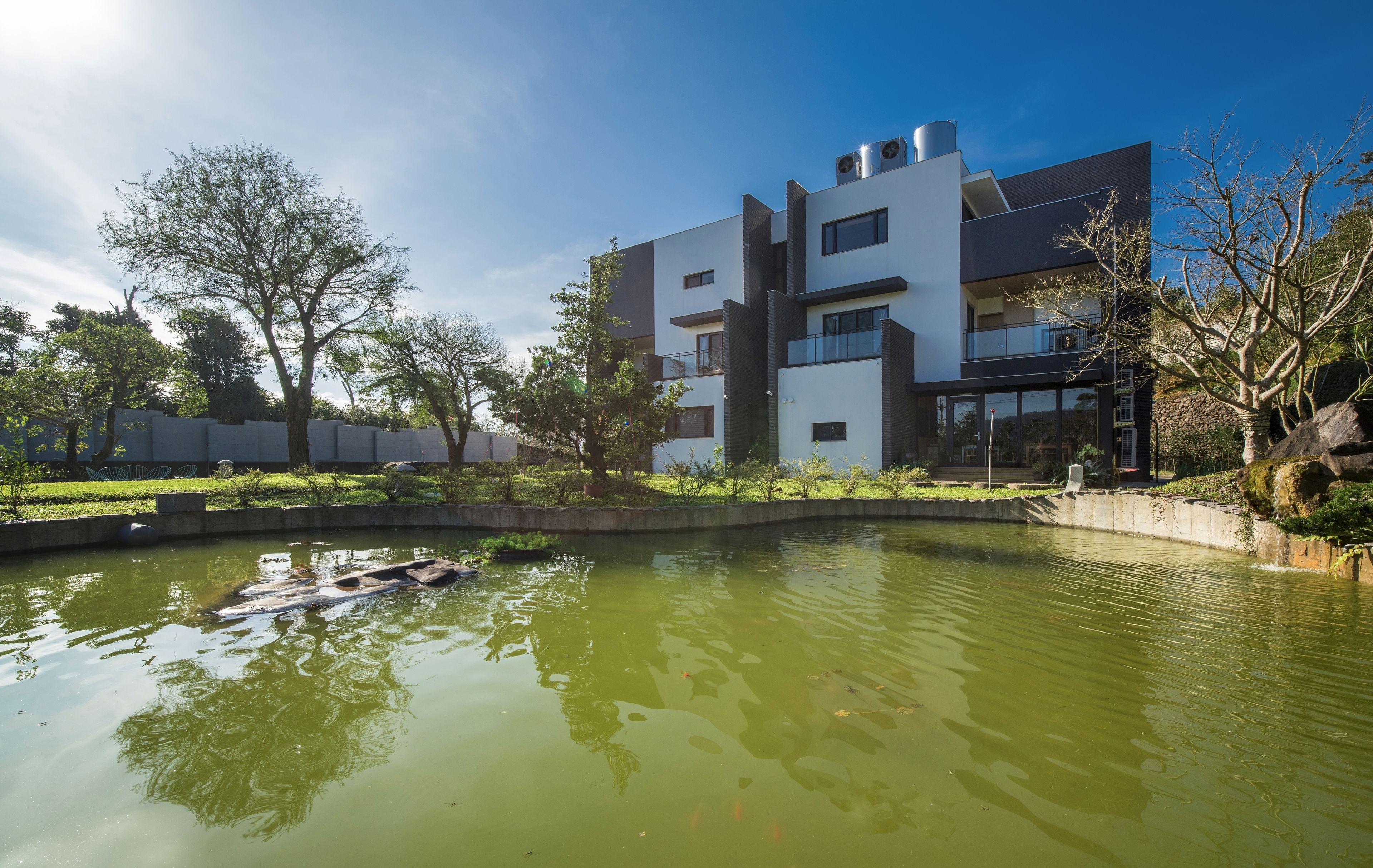 Un edificio moderno con piscina en la azotea, rodeado de vegetación y árboles.