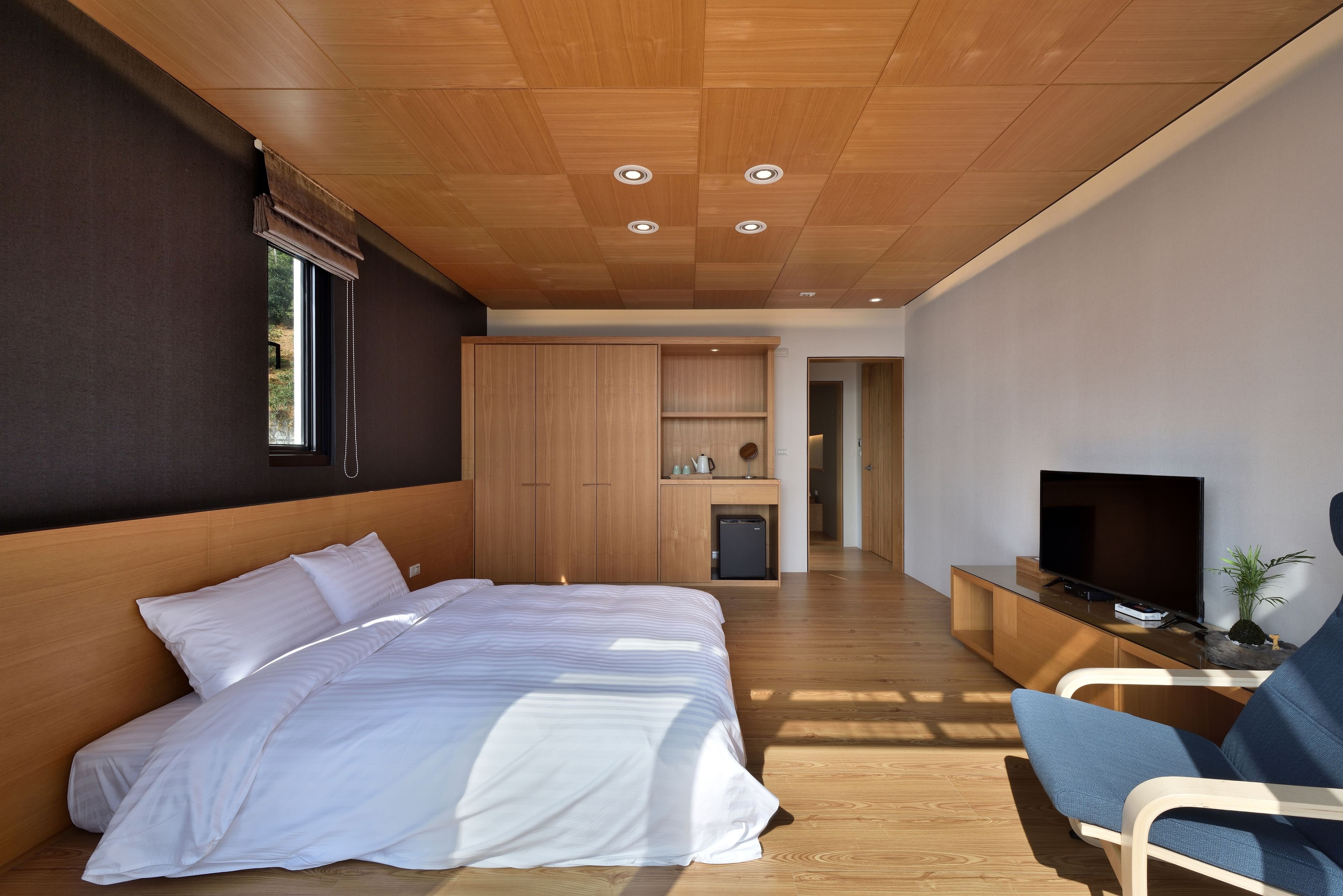 A modern bedroom with a large bed, wooden ceiling, built-in wardrobe, and a TV on a wooden console.