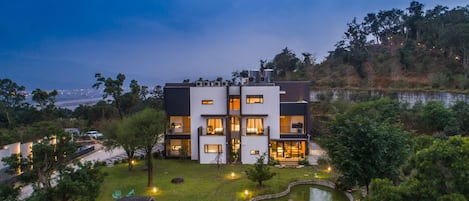 A modern multi-story house with a well-maintained garden, including a pond and outdoor seating.