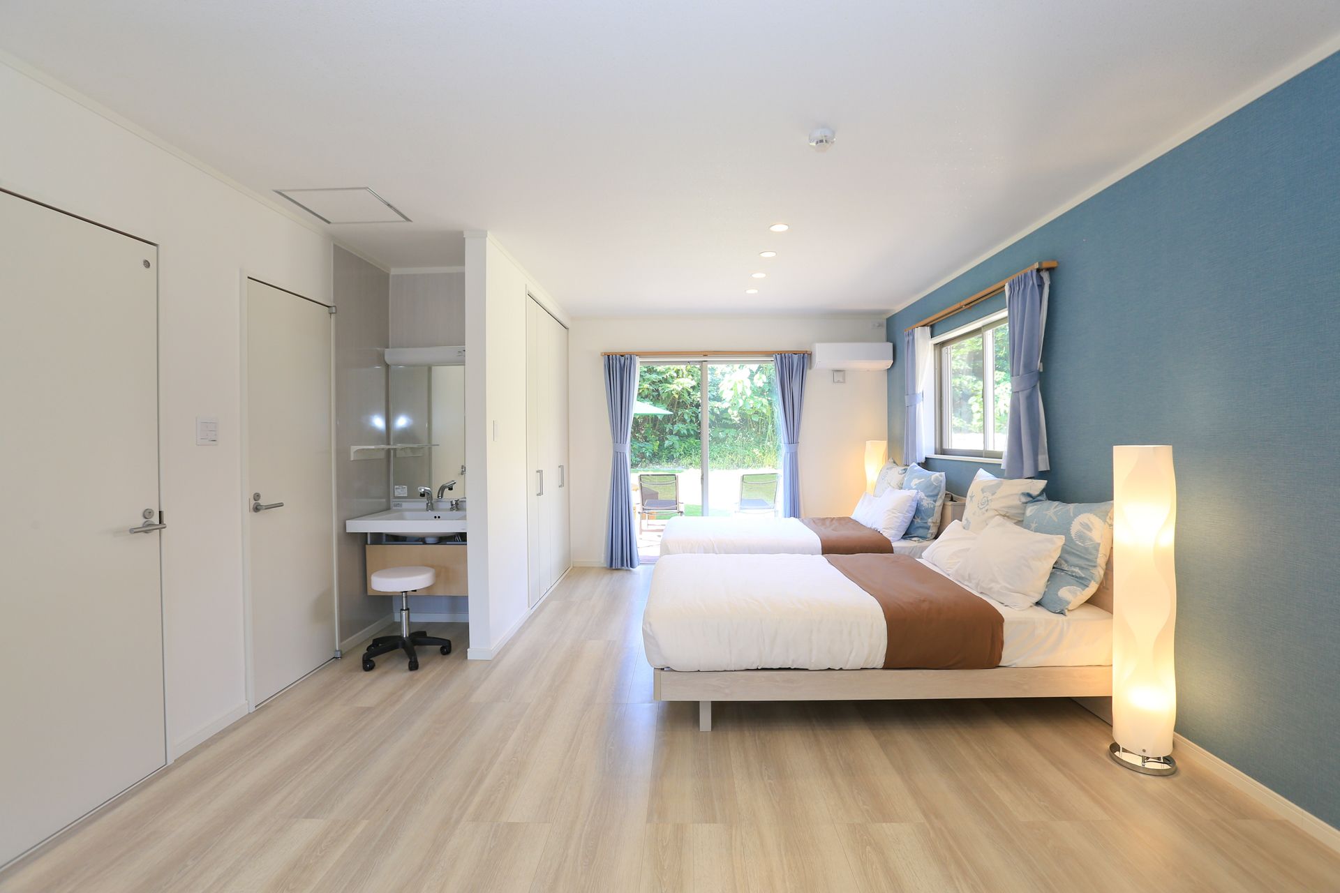 A modern bedroom with a large bed, a bedside table, a mirror, and a view of the outdoors.