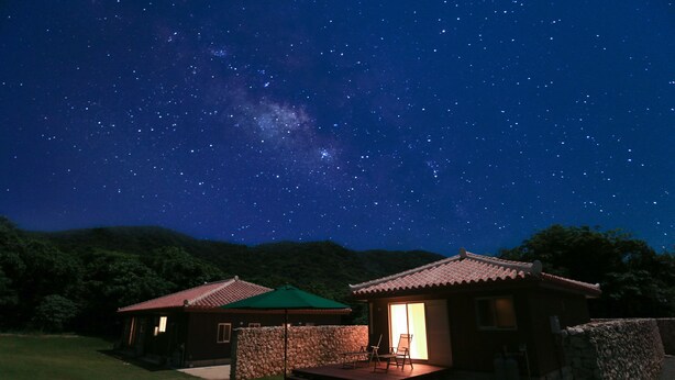 A night scene with a starry sky, two buildings with traditional architecture, and a grassy area with outdoor furniture. - Stardust Villa Milky Way (Ishigaki)