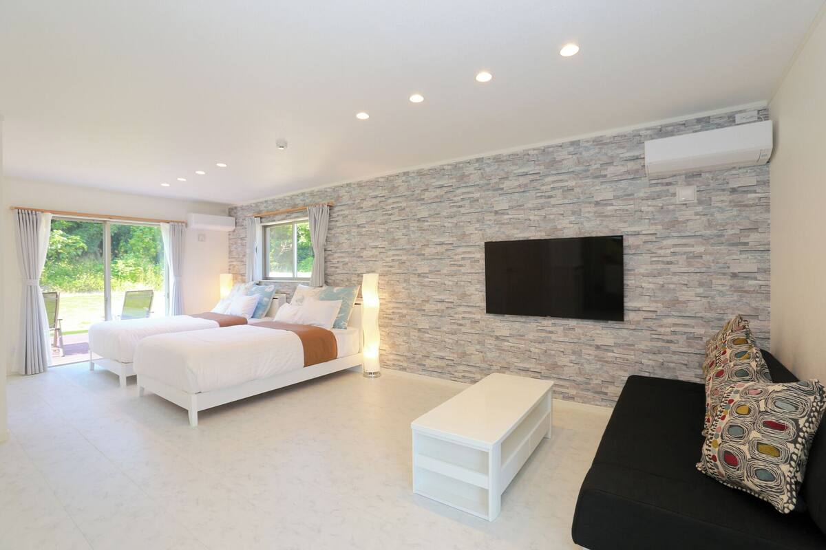 Un dormitorio moderno con dos camas, un televisor y un ventanal grande.