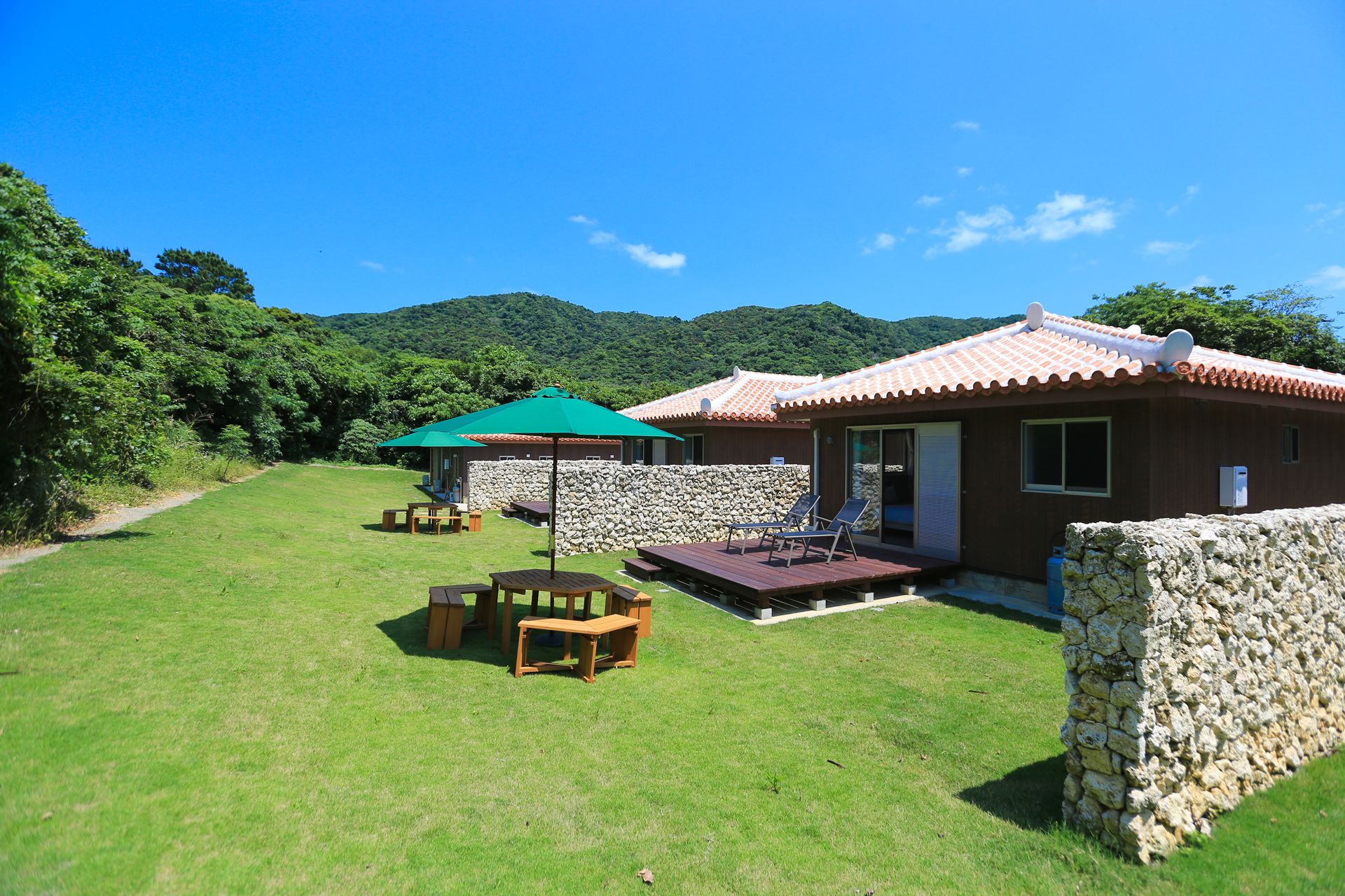 A traditional-style building with a stone wall, a patio with wooden furniture, and a green umbrella.