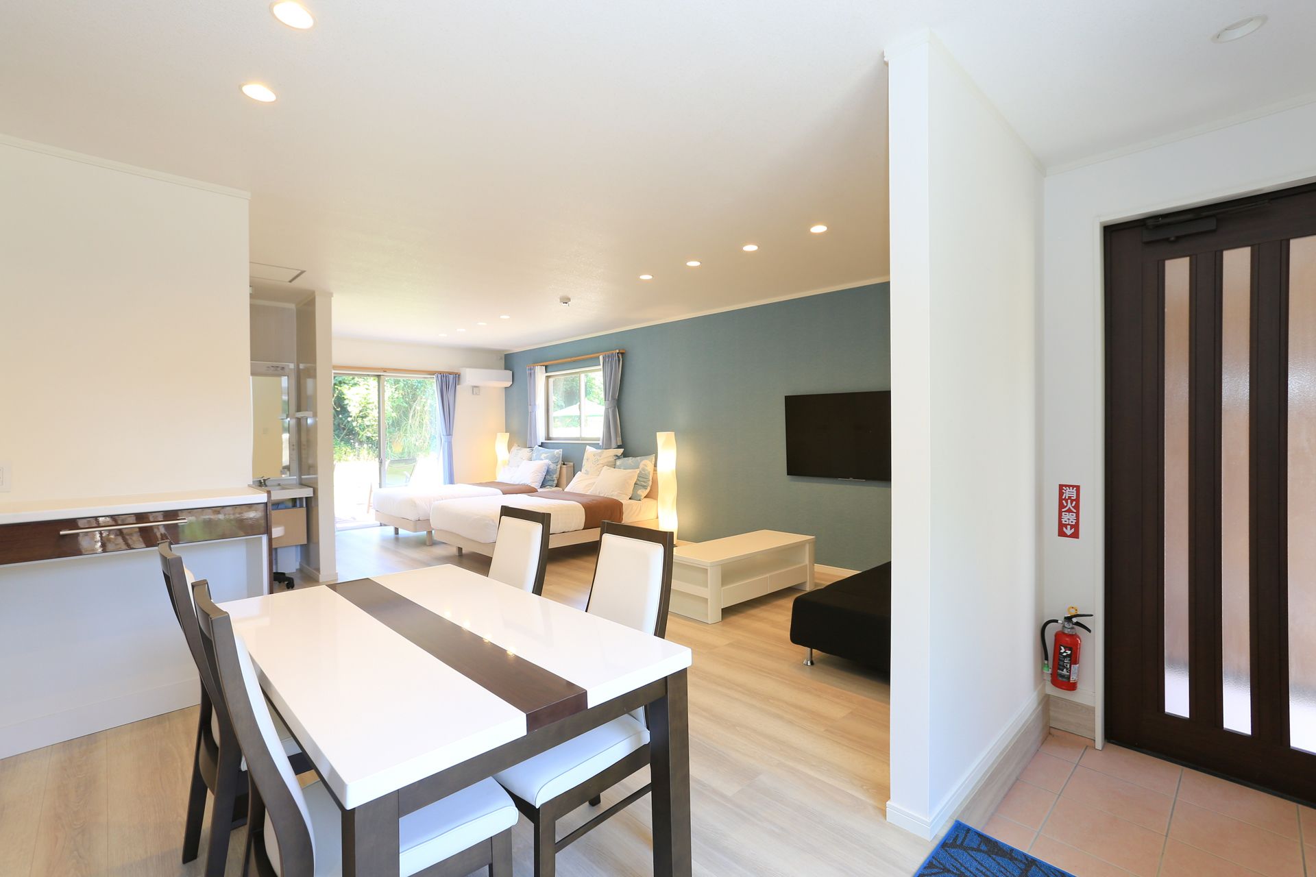 A modern hotel room with a dining area, a bed, a TV, and a fire extinguisher.