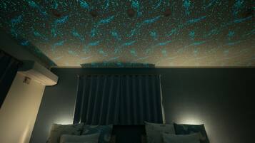 A room with a bed, a window with curtains, and a ceiling with a star projection.