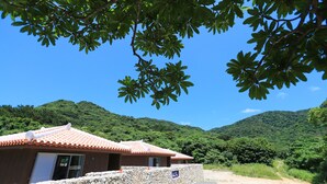 A traditional building with a tiled roof and stone walls, surrounded by lush greenery and hills. - Stardust Villa Milky Way (Ishigaki)