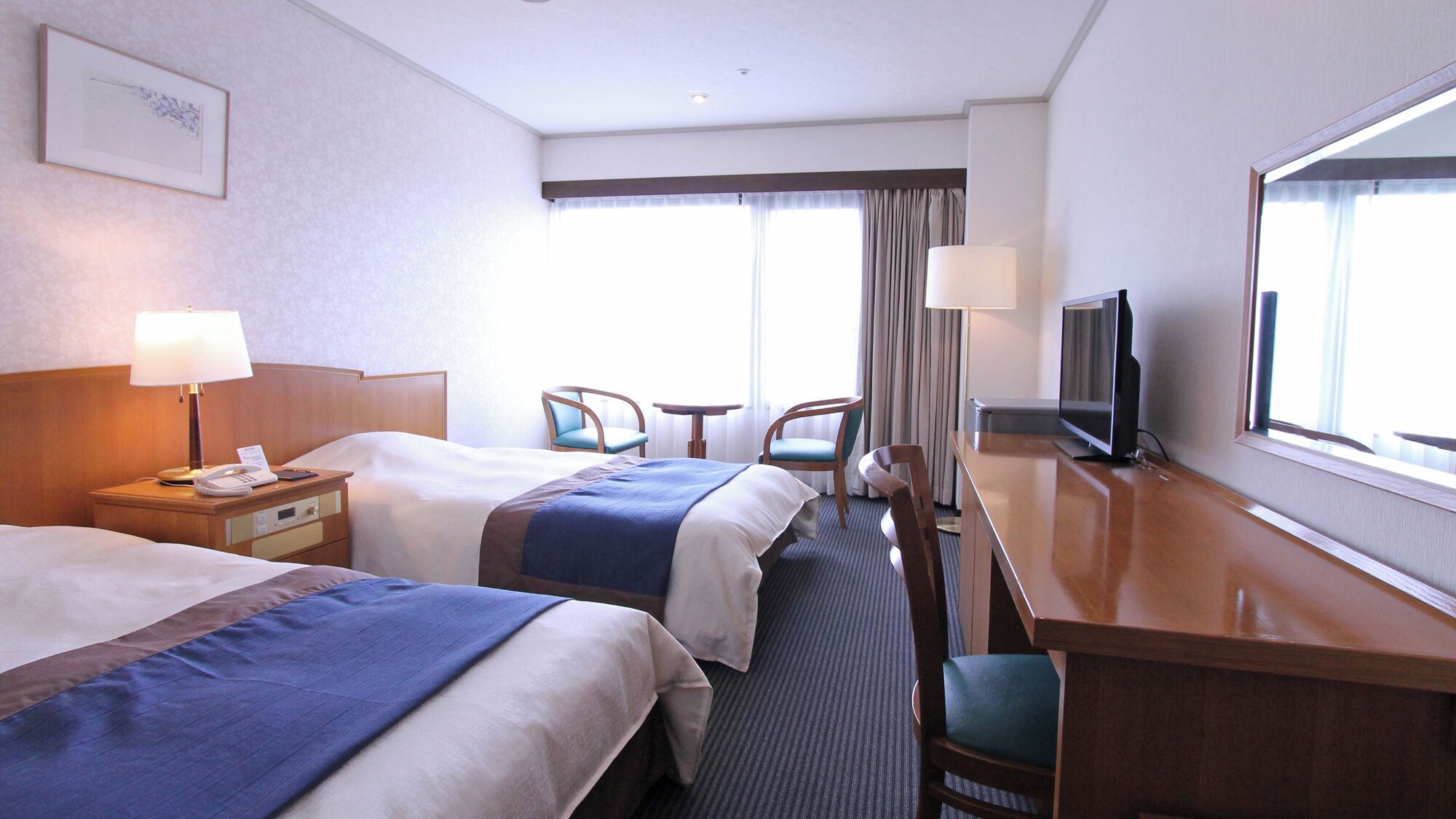 A hotel room with two beds, a desk with a TV, a chair, a lamp, and a window with curtains.